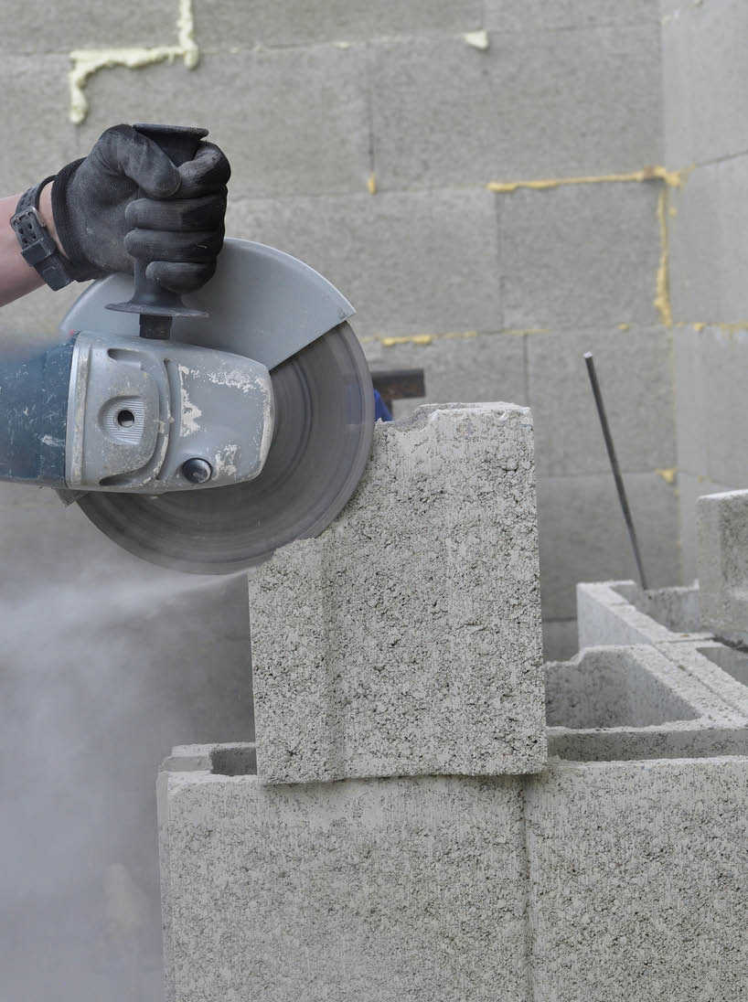 View of a mason's hands on a construction site sawing a block using an electric grinder