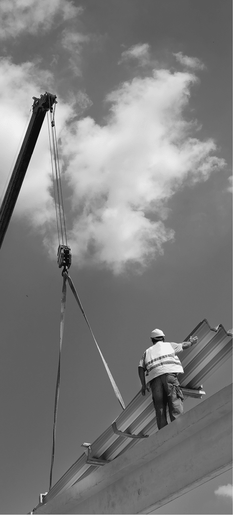 Construction worker standing on concrete beam on height and placing roof materials lifted by crane