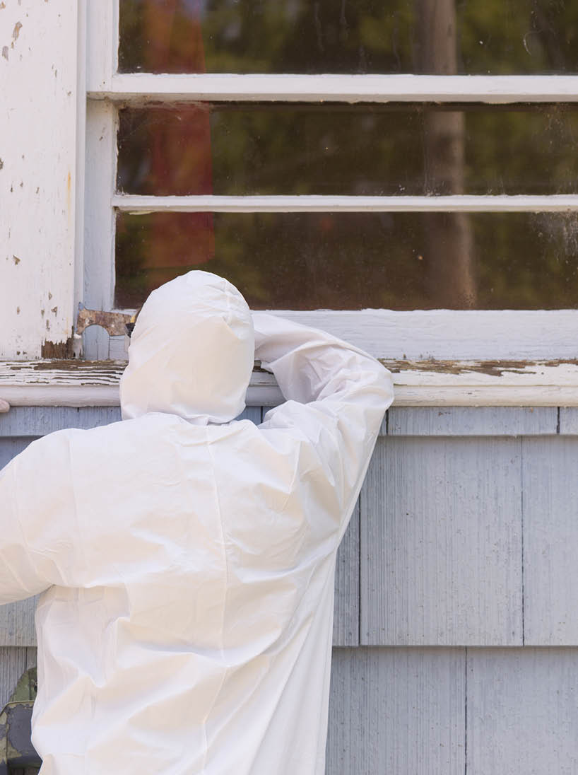 A house painter in a hazmat suit scrapes off dangerous lead paint from a window sill 