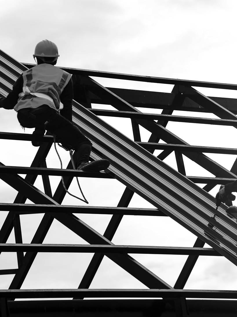 Construction engineer wear safety uniform using an electric drill and screw tools to fasten down metal roofing work for roof industrial concept with copy space