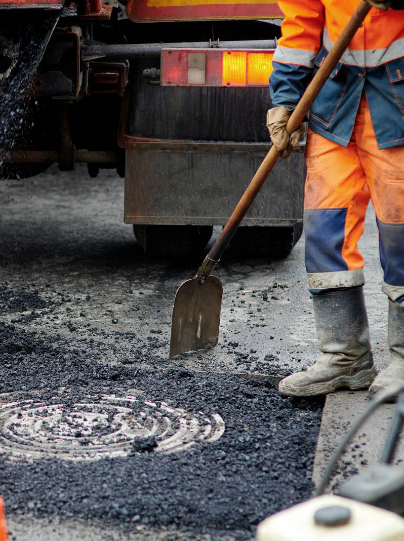 Construction worker in uniform operate vibratory plate compactor  Pothole repair process  Asphalt tamping machine operator  Pothole patching and repair  Laying asphalt around the hatch  New asphalt