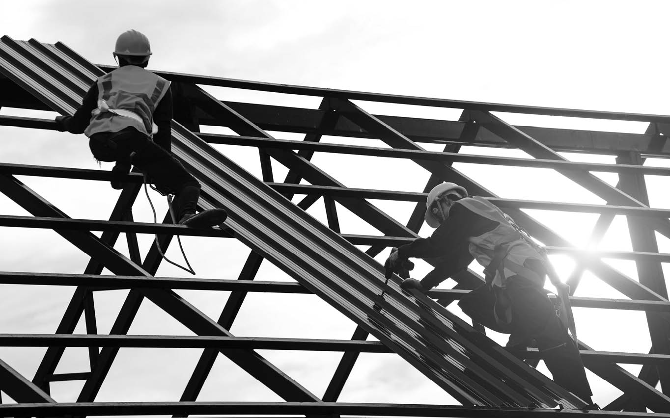 Construction engineer wear safety uniform using an electric drill and screw tools to fasten down metal roofing work for roof industrial concept with copy space